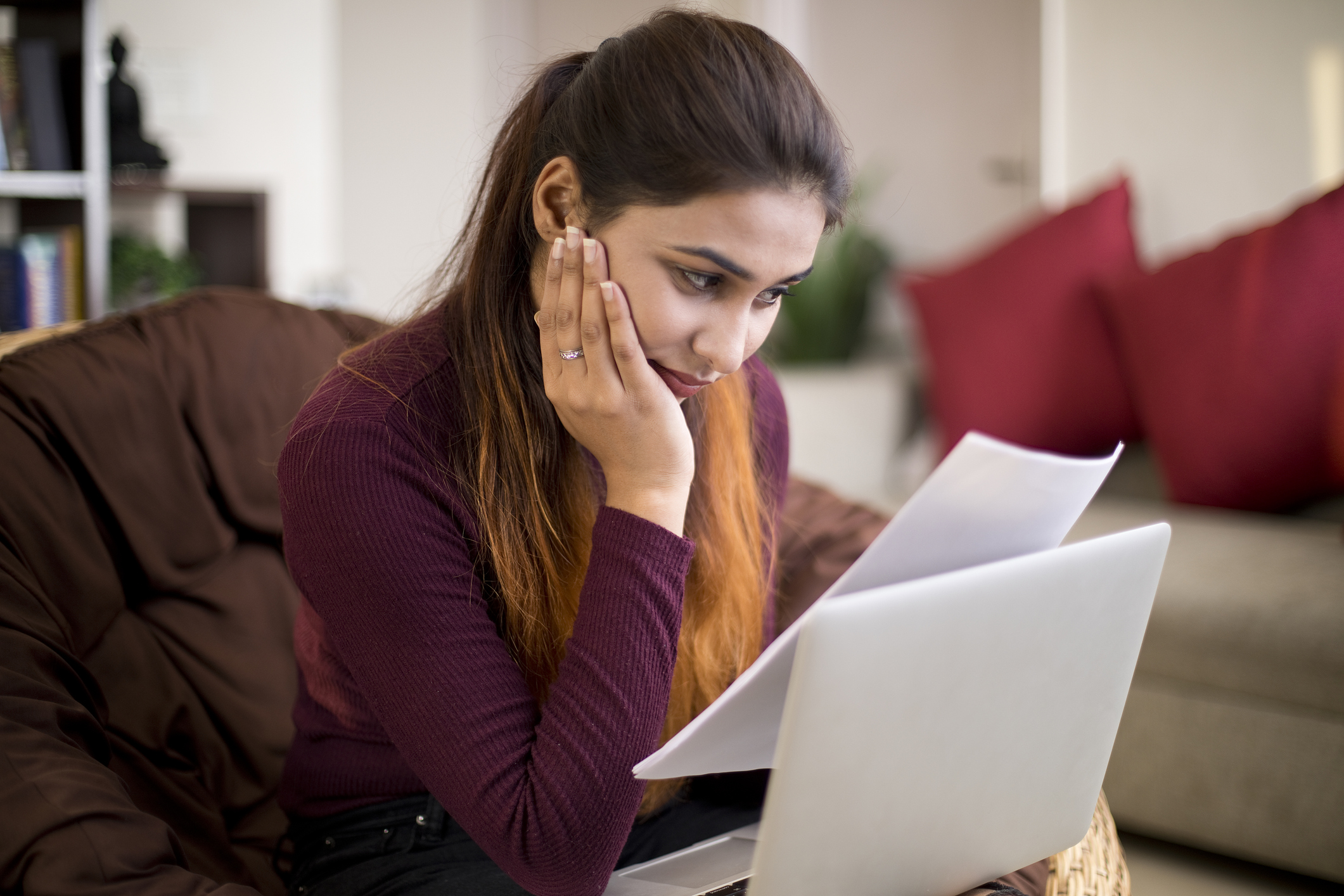 Female college graduate sitting on a couch at home going through her student loan bills with a worried look on her face.